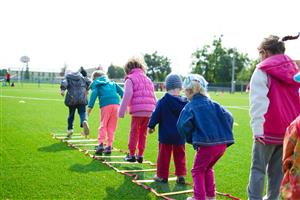 Young children jumping through a ladder drill on an athletic field